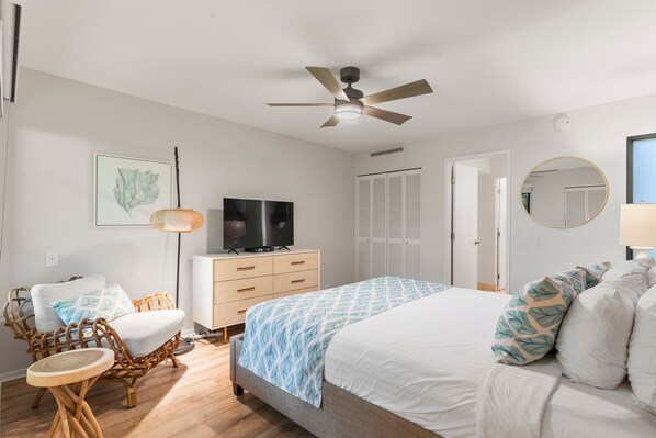 A bedroom with a bed, a TV, a ceiling fan, a wardrobe, and a chair.