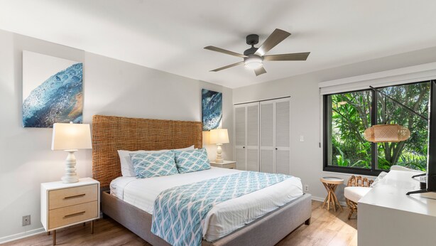 A modern bedroom with a bed, bedside tables, a ceiling fan, and a window with a view of greenery. - Wailea Elua, #0801 2 Bedroom Condo by RedAwning (Kihei)
