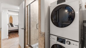 A laundry area with stacked washing machines and a glass door leading to a bedroom. - Wailea Elua, #0801 2 Bedroom Condo by RedAwning (Kihei)