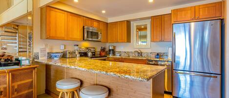 A modern kitchen with wooden cabinets, a stainless steel refrigerator, and a granite countertop.