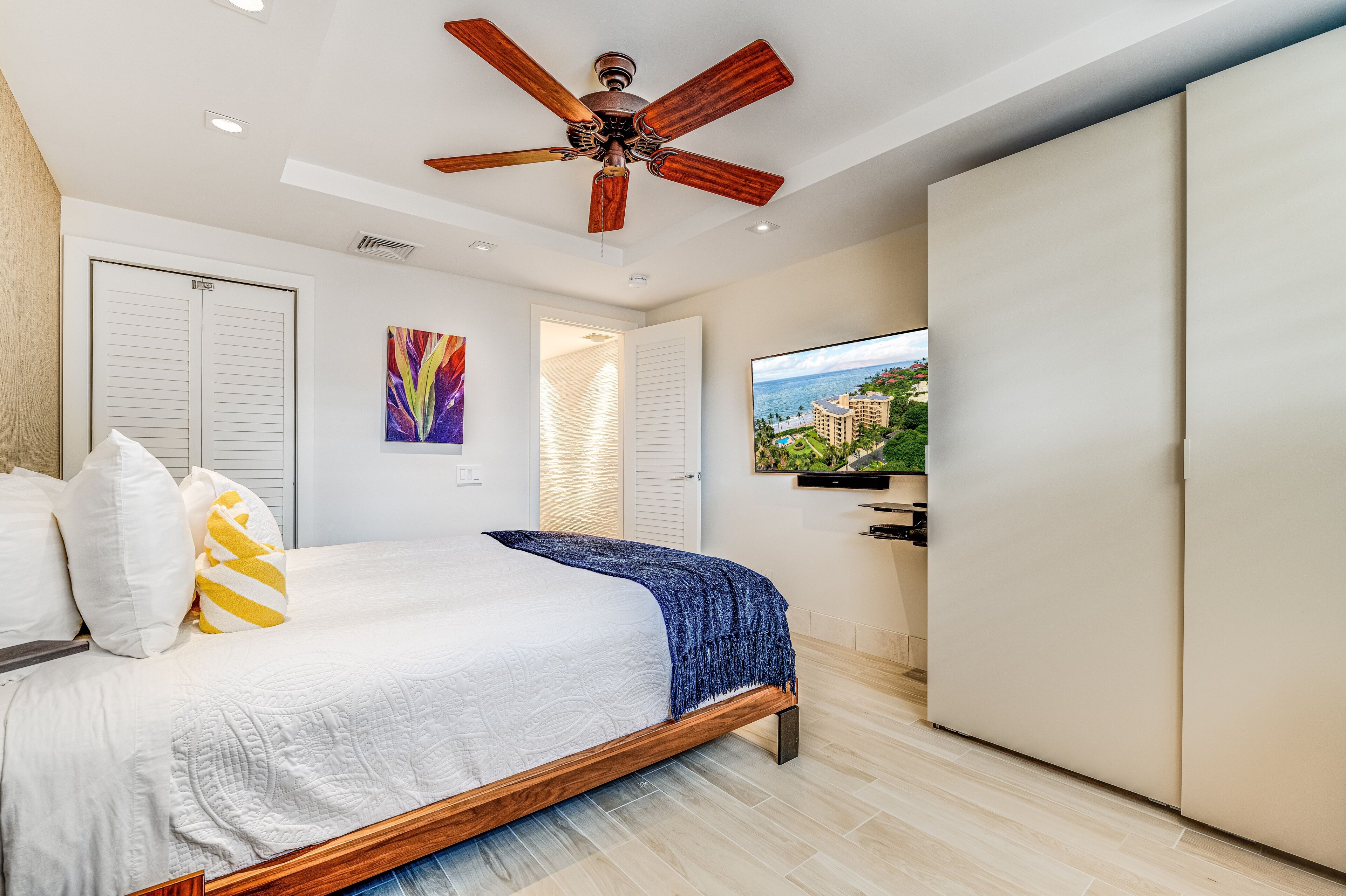 A bedroom with a bed, a ceiling fan, a TV, and a wardrobe.