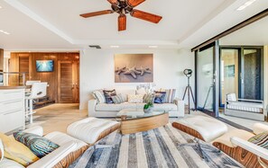 A modern living room with a ceiling fan, a large window, and a dining area with a wooden cabinet. - Polo Beach Club, #707 2 Bedroom Condo by RedAwning (Kihei)