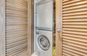 A compact, modern laundry room with a built-in washer and dryer, enclosed by wooden panel walls. - Polo Beach Club, #707 2 Bedroom Condo by RedAwning (Kihei)