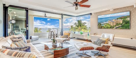 A spacious living room with a balcony, modern furniture, and a large window offering a view of the ocean.