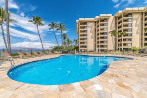 A swimming pool with lounge chairs and palm trees, surrounded by a multi-story building with balconies. - Polo Beach Club, #707 2 Bedroom Condo by RedAwning (Kihei)