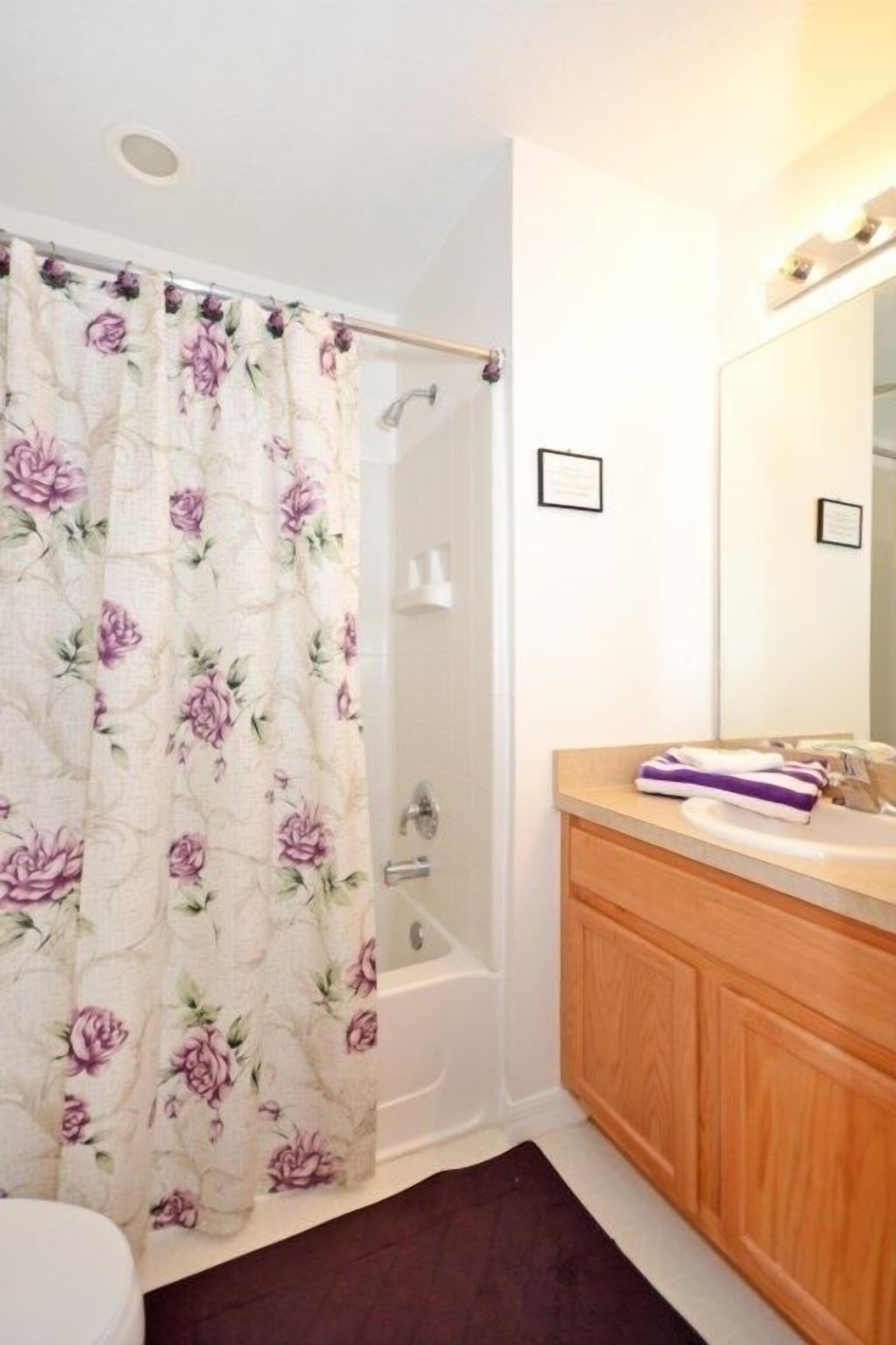 Une salle de bain avec un rideau de douche, une baignoire, un meuble-lavabo en bois et un miroir.