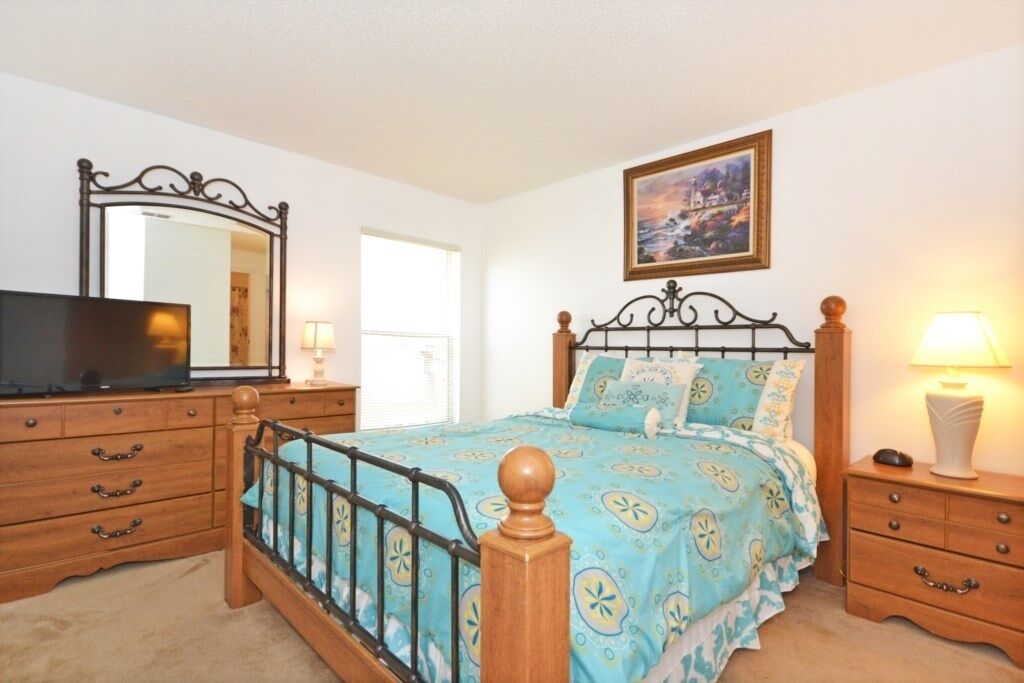 A bedroom with a bed, a dresser, a TV, and a painting on the wall.