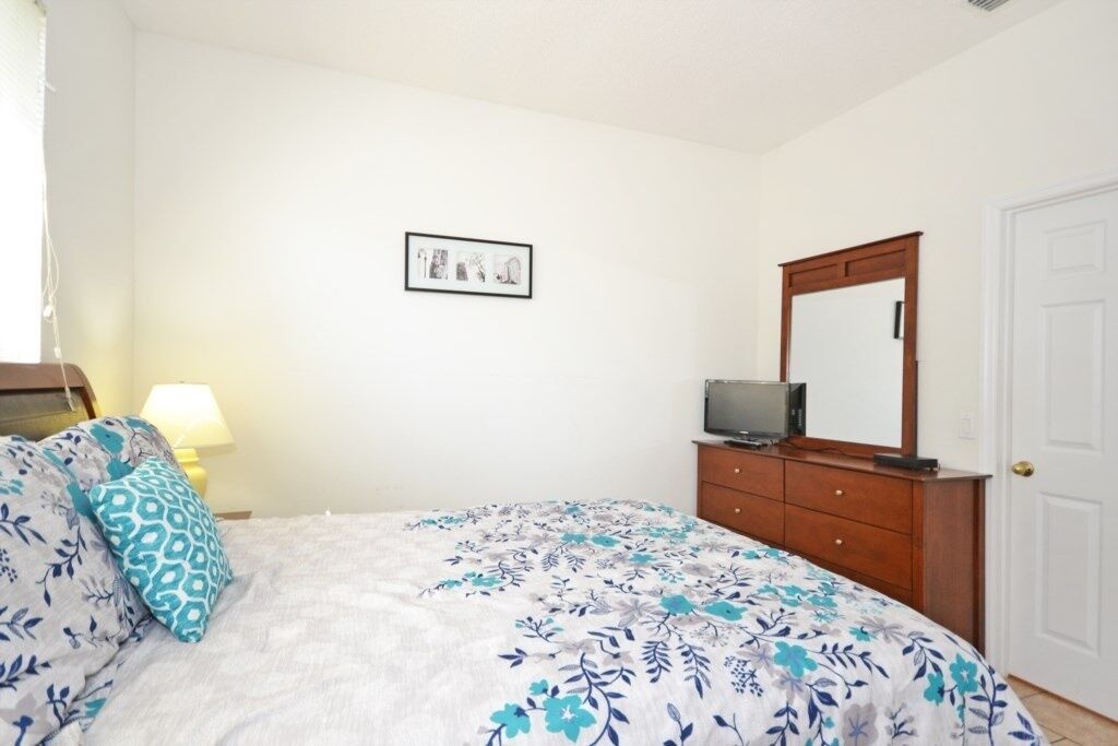 A bedroom with a bed, a dresser, a television, and a framed picture on the wall.