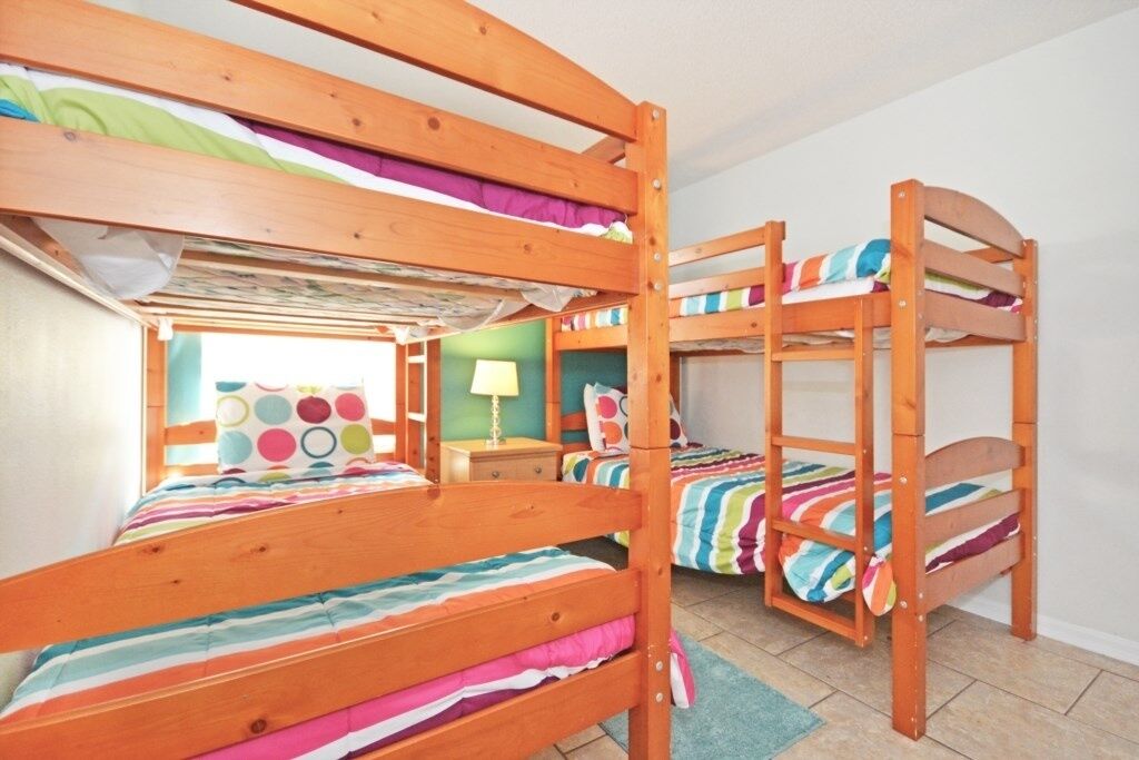 A bunk bed room with a window, a lamp, and a colorful striped bedspread.