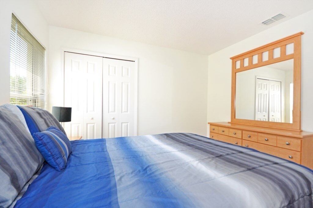A bedroom with a bed, a dresser, a mirror, and a door.