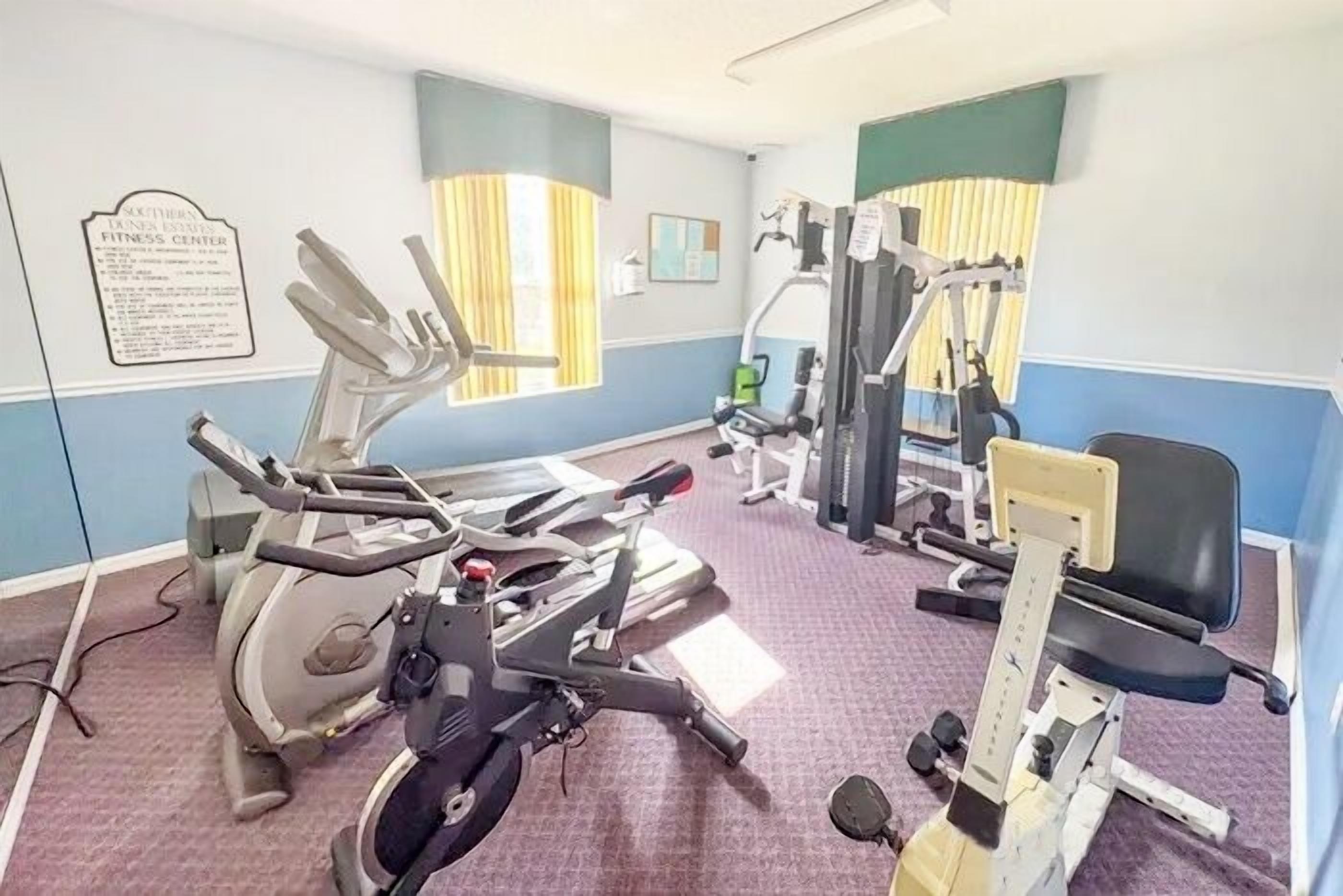 A fitness center with cardio machines, weight training equipment, and a bulletin board.