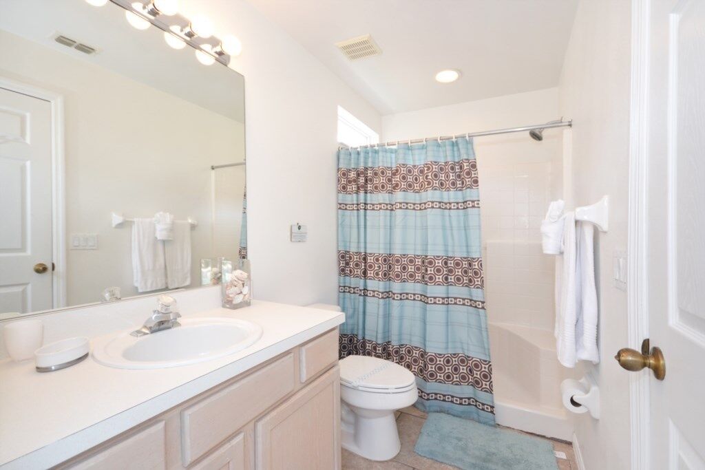 A bathroom with a white sink, a toilet, a shower curtain, and a mirror with lights.