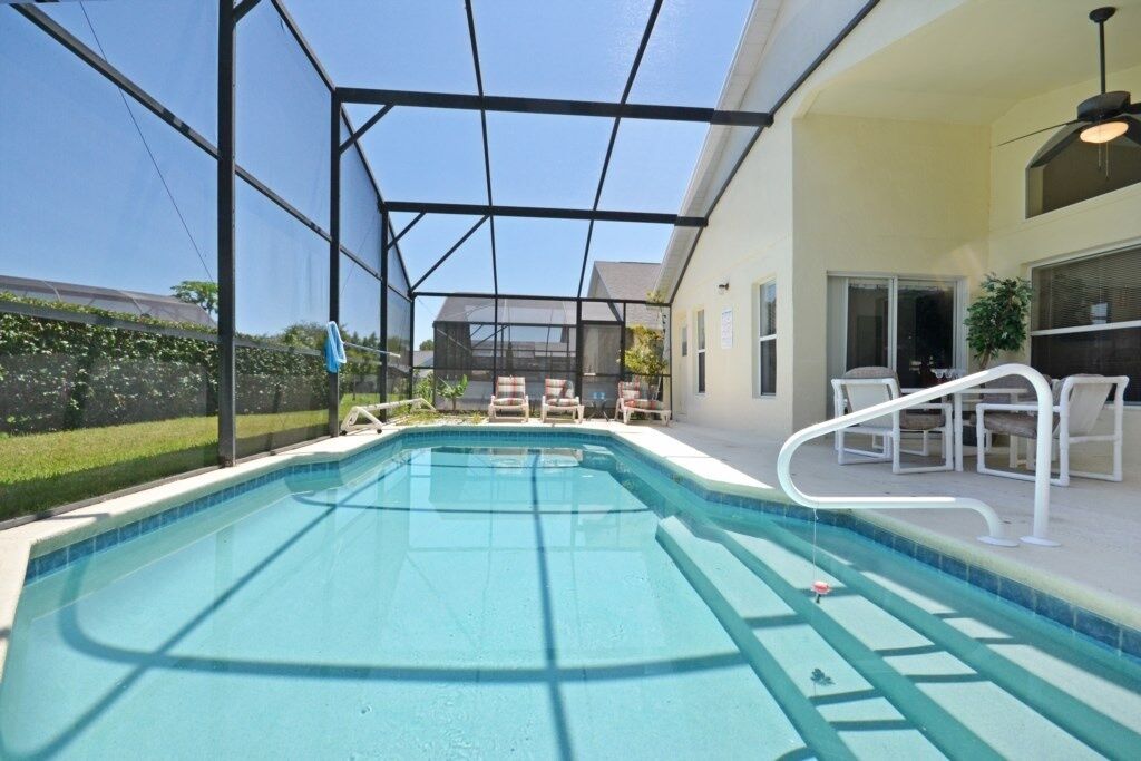 A swimming pool with a glass enclosure, surrounded by outdoor furniture and a covered patio area.