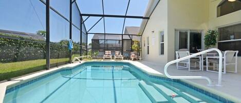 A swimming pool with a glass enclosure, surrounded by outdoor furniture and a covered patio area.