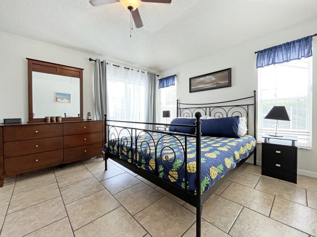 A bedroom with a bed, a dresser, a ceiling fan, and a window with curtains.