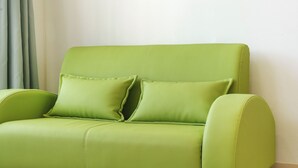 Um sofá estofado verde com duas almofadas, encostado a uma parede lisa.