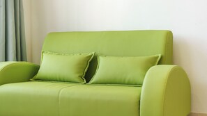 A green upholstered sofa with two cushions against a plain wall. - Gangleung Laimbichipensyeon (Gangneung)