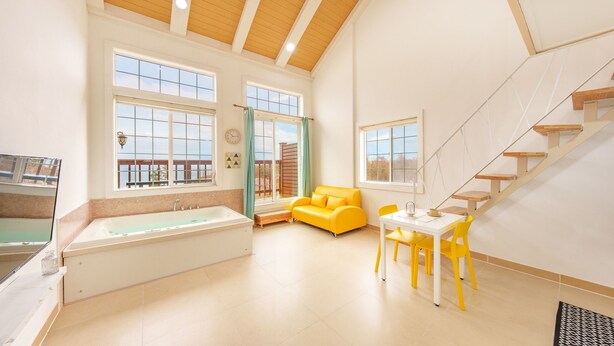 A spacious room with a large bathtub, a yellow sofa, and a dining area with yellow chairs. - Gangleung Laimbichipensyeon (Gangneung)