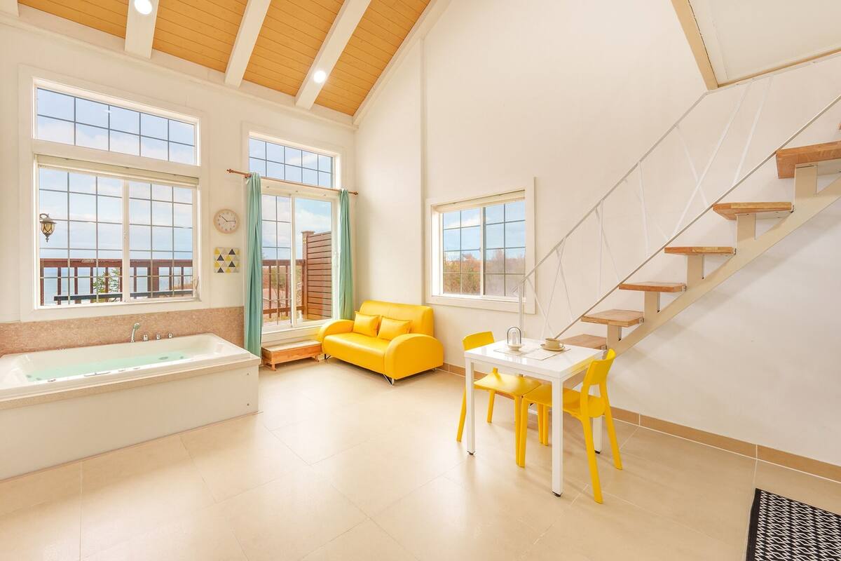 A spacious room with a large bathtub, a yellow sofa, and a dining area with yellow chairs.