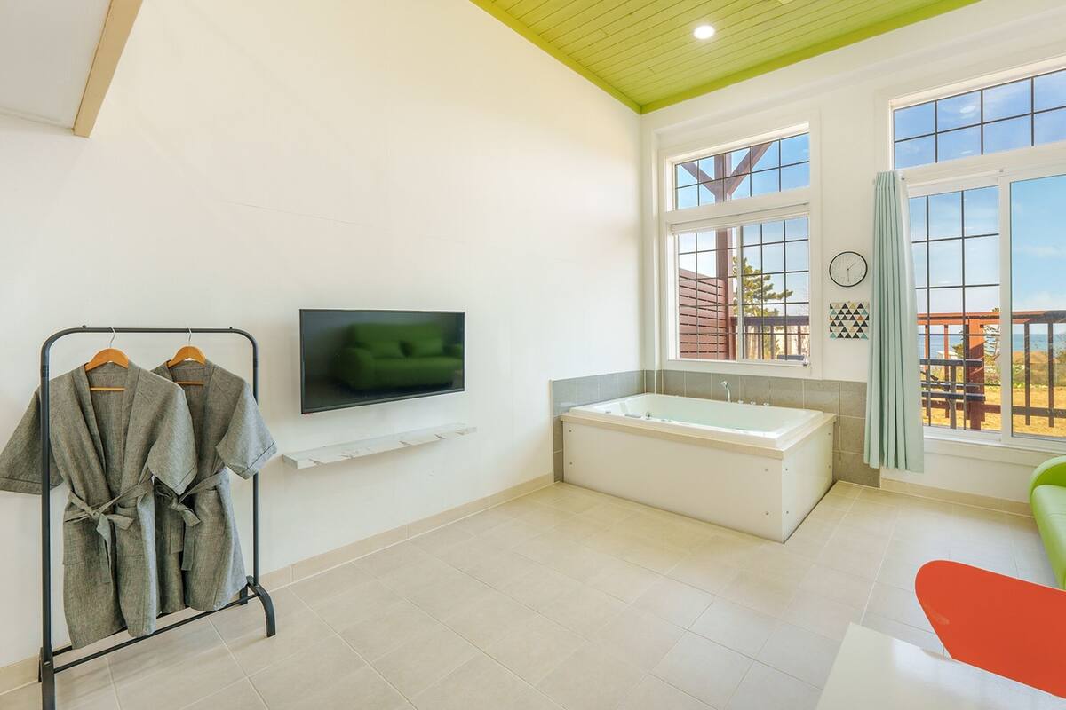 A modern bathroom with a bathtub, a green sofa, and a TV mounted on the wall.