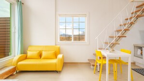 A bright yellow sofa and chairs in a room with a view of mountains through a window. - Gangleung Laimbichipensyeon (Gangneung)