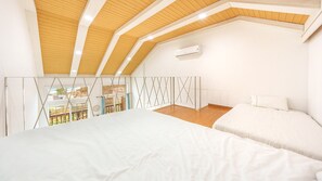 A bedroom with a sloped ceiling, wooden beams, a bed, and an air conditioning unit. - Gangleung Laimbichipensyeon (Gangneung)