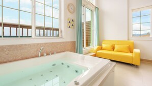 Un baño con una bañera grande, un sofá amarillo y un ventanal con vistas.