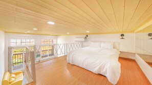 Un dormitorio con una cama grande, suelo de madera, un balcón con barandilla y un equipo de aire acondicionado en la pared.
