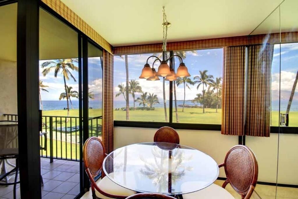 A room with a glass table and chairs, a view of a golf course, and a hanging light fixture.