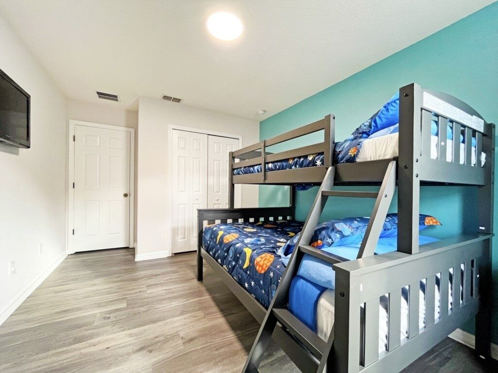 A bunk bed room with a wooden floor, white doors, and a teal accent wall.
