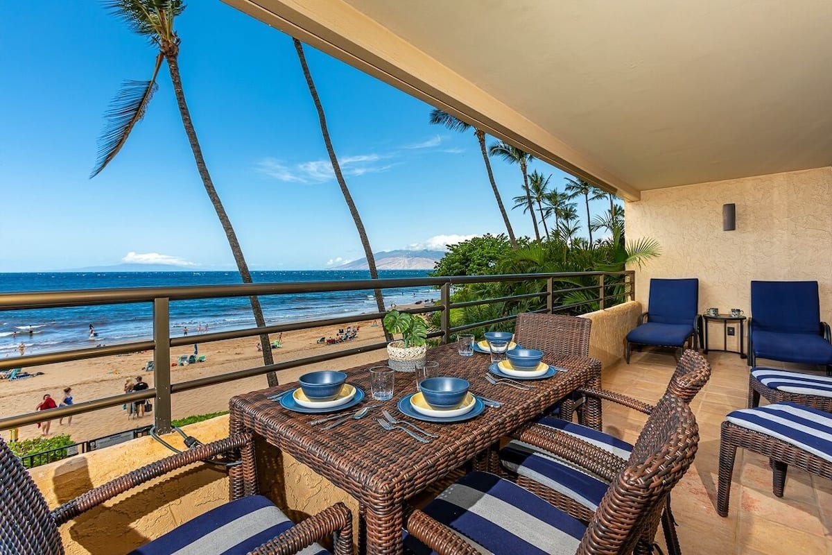 Ein Balkon mit Korbmöbeln, einem Esstisch und Blick auf Strand und Meer.