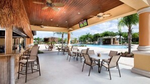 Une terrasse extérieure avec des chaises et des tables, une piscine et une structure surmontée d’un toit de chaume.