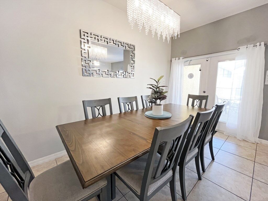 A dining area with a wooden table and six chairs, a decorative mirror, and a chandelier.