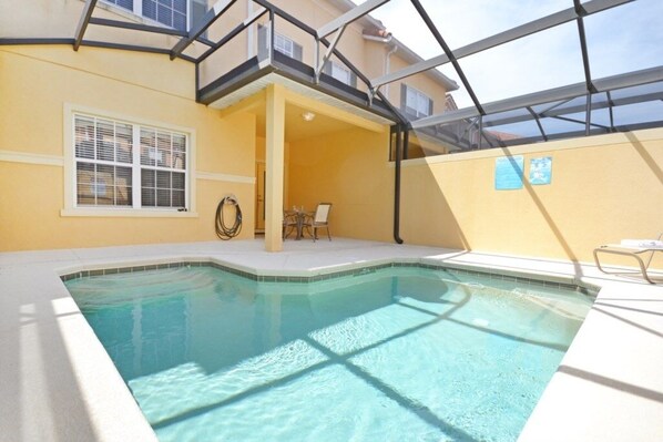 Una piscina con techo de vidrio, una silla y una mesita.