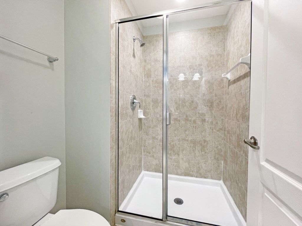 A glass-enclosed shower stall with a white tiled floor and a visible drain.