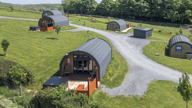 A series of dome-shaped cabins with a gravel path connecting them, surrounded by lush greenery and hills. - Cherry (Ulverston)