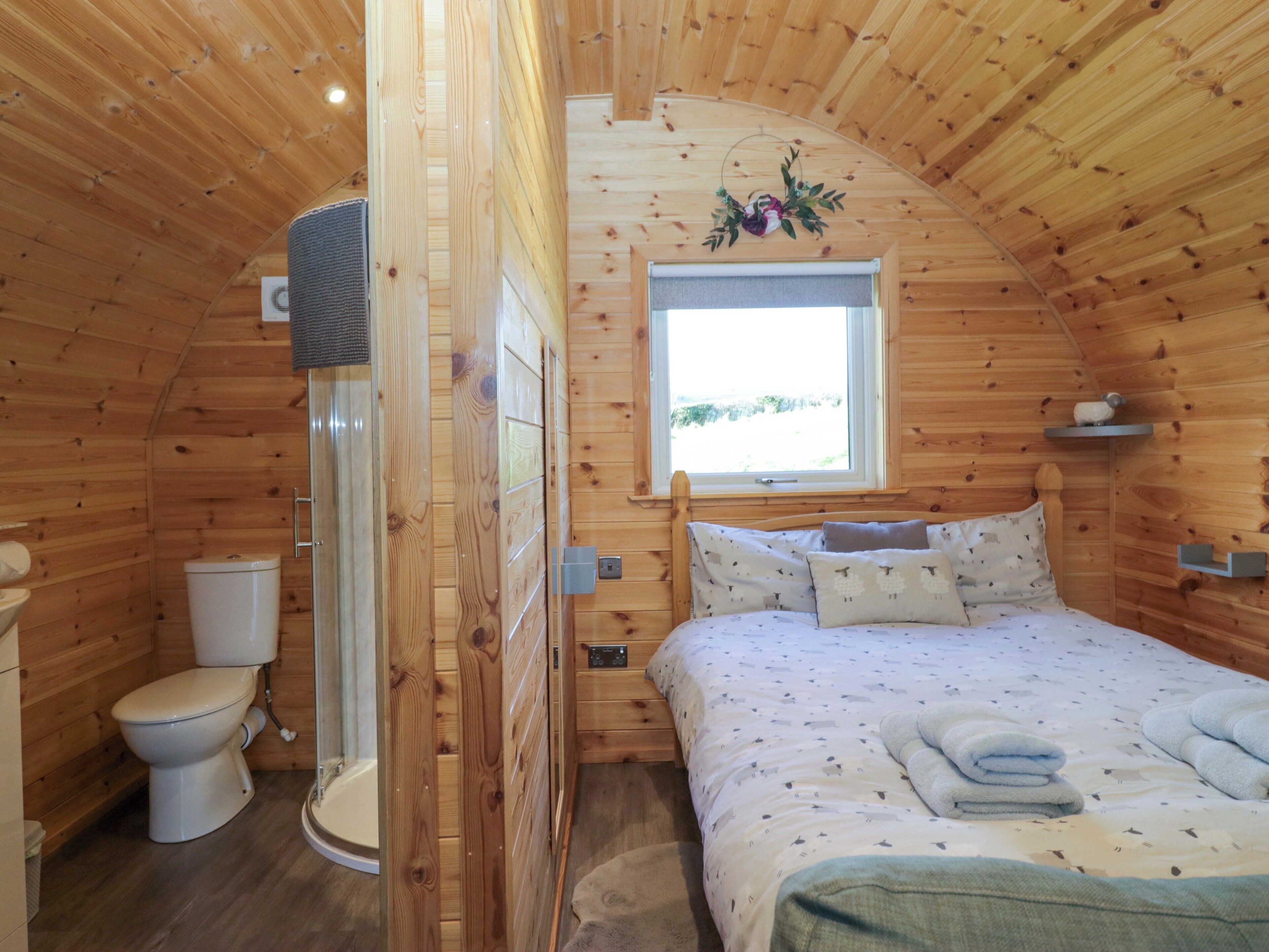 A wooden cabin bedroom with a bed, pillows, a window, and a toilet.