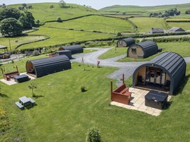 Un entorno rural con varias cabañas pequeñas y techos curvos, cada una con un patio y vistas del paisaje verde circundante.