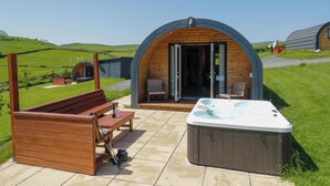 A cozy outdoor area with a wooden bench, a hot tub, and a wooden structure with an open door. - Cherry (Ulverston)