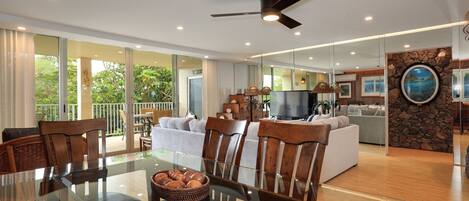 A spacious living area with a glass dining table, wooden chairs, and a ceiling fan.