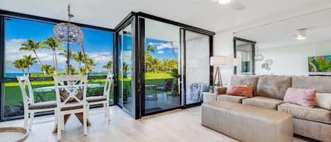 A spacious living area with a large sliding glass door leading to a balcony, a sofa, and a dining table with chairs.