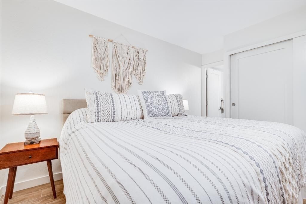 A bedroom with a bed, a nightstand, a wall hanging, and a door.