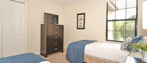 A bedroom with two beds, a dresser, a window with blinds, and a framed picture on the wall.