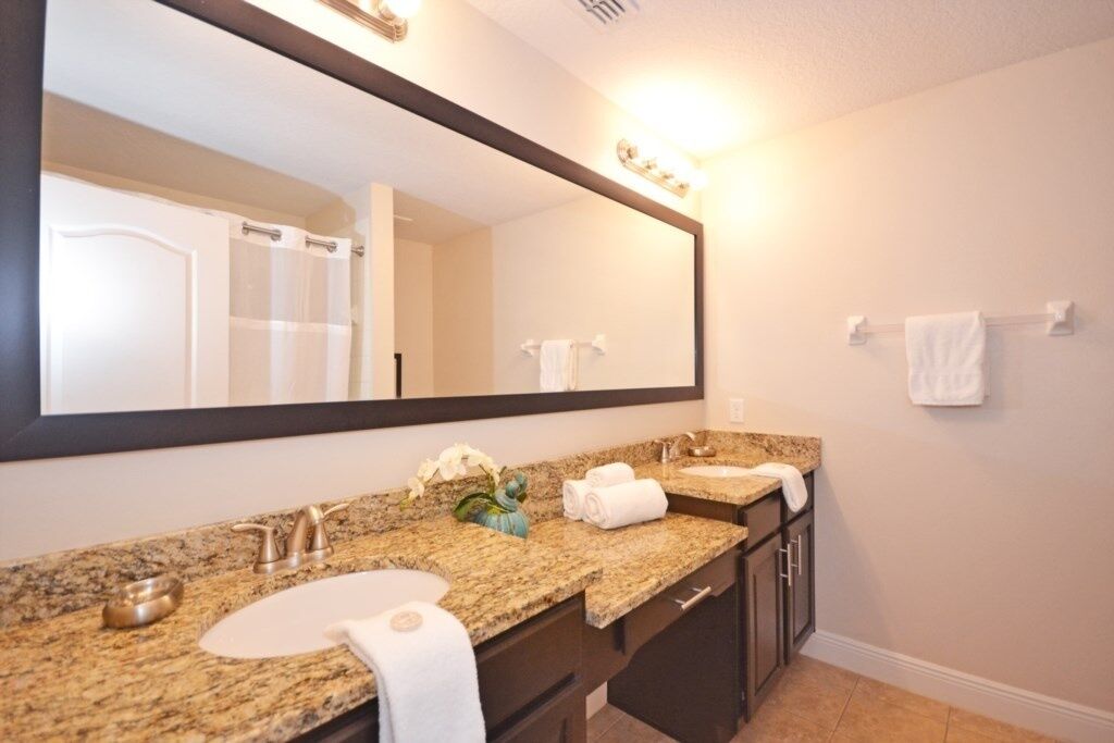 A bathroom with a granite countertop, two sinks, a large mirror, and a towel rack.