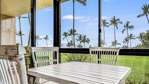 A white table and chairs in a room with large windows overlooking a lawn with palm trees. - Kihei Surfside, #113 1 Bedroom Condo by RedAwning (Kihei)