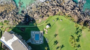 An aerial view of a resort with a swimming pool, palm trees, and rocky terrain. - Kihei Surfside, #113 1 Bedroom Condo by RedAwning (Kihei)