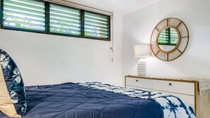 A bedroom with a bed, a dresser, a mirror, and a window with blinds. - Kihei Surfside, #113 1 Bedroom Condo by RedAwning (Kihei)