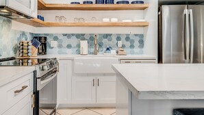 A modern kitchen with white cabinetry, a stainless steel refrigerator, a built-in oven, and a coffee machine. - Kihei Surfside, #113 1 Bedroom Condo by RedAwning (Kihei)