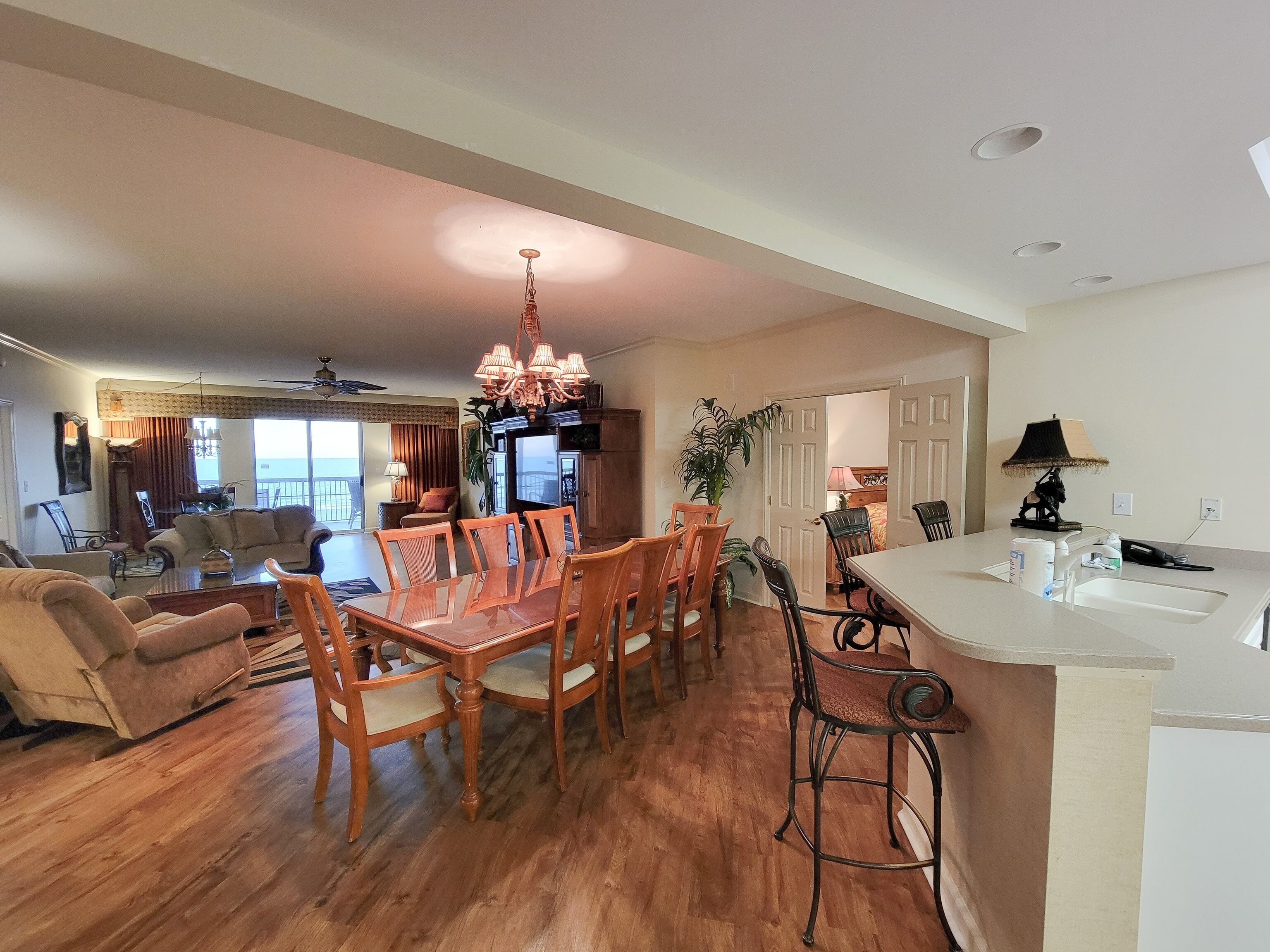 A spacious living area with a dining table and chairs, a kitchen with a bar, and a balcony with a view.
