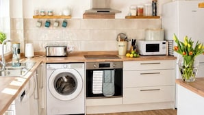 A compact kitchen with a washing machine, microwave, and wooden countertop.
